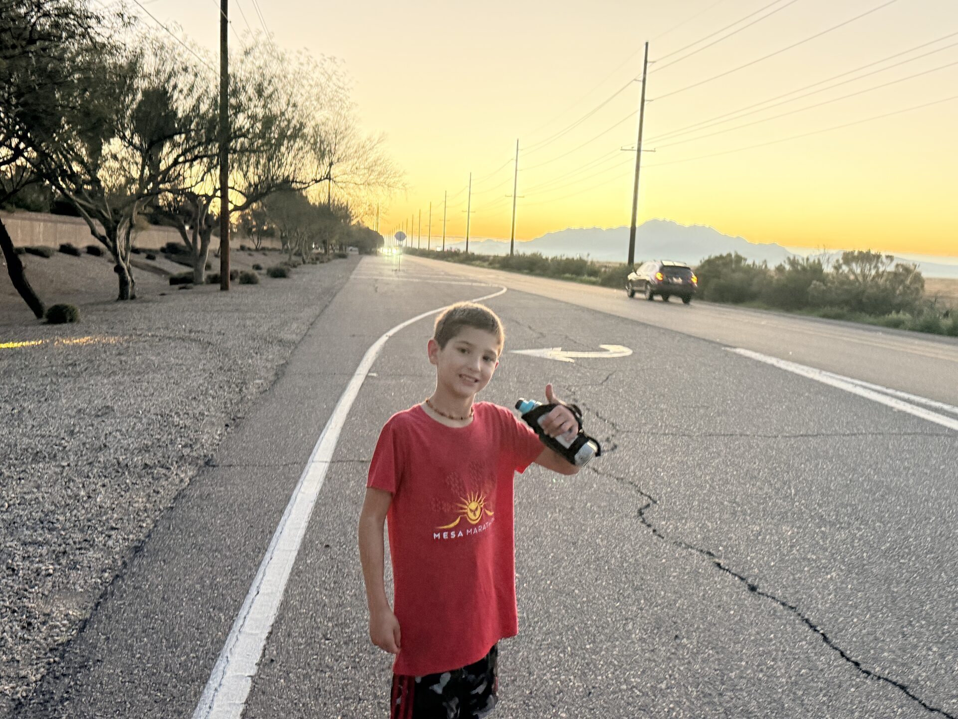 Atlas, 10, giving the thumbs up on Hunt Highway with the sunrise behind him